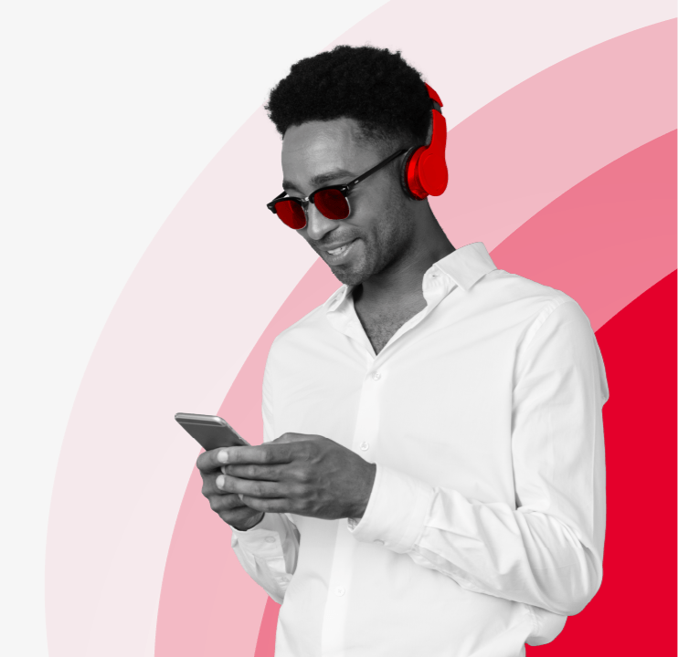 A man in a white shirt smiling down at a phone, wearing red glasses and red headphones